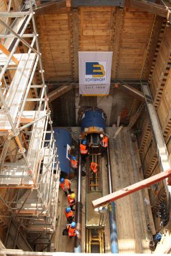 Blick in den Schacht mit dem Ende der Vortriebsmascine (oben) und dem starken Hydrailikgestänge, das die Stahlrohre in die Tunnelbohrung schieben wird. Foto: Ralf Julke