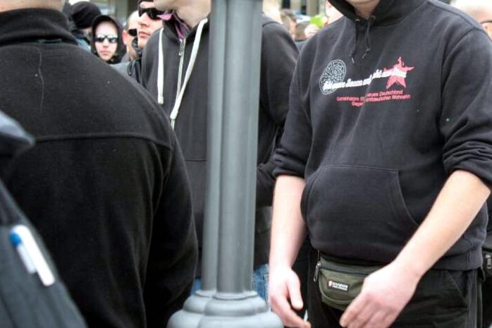 Hübsche Symbole hinter dem Fronttransparent - das Zeigen der schwarzen Sonne in politischen Zusammenhängen ist in Deutschland verboten