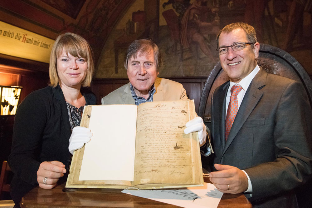 Bernhard Rothenberger (r.), Pächter des Auerbachs Keller, Haushistoriker Bernd Weinkauf und Anke Beesch, Objektmanagerin Mädler Passage, mit dem historischen Band: das zurückgekehrte Fremdenbuch (Gästebuch) mit Einträgen aus den Jahren 1859 bis 1866. Foto: Christian Modla/Abdruck honorarfrei