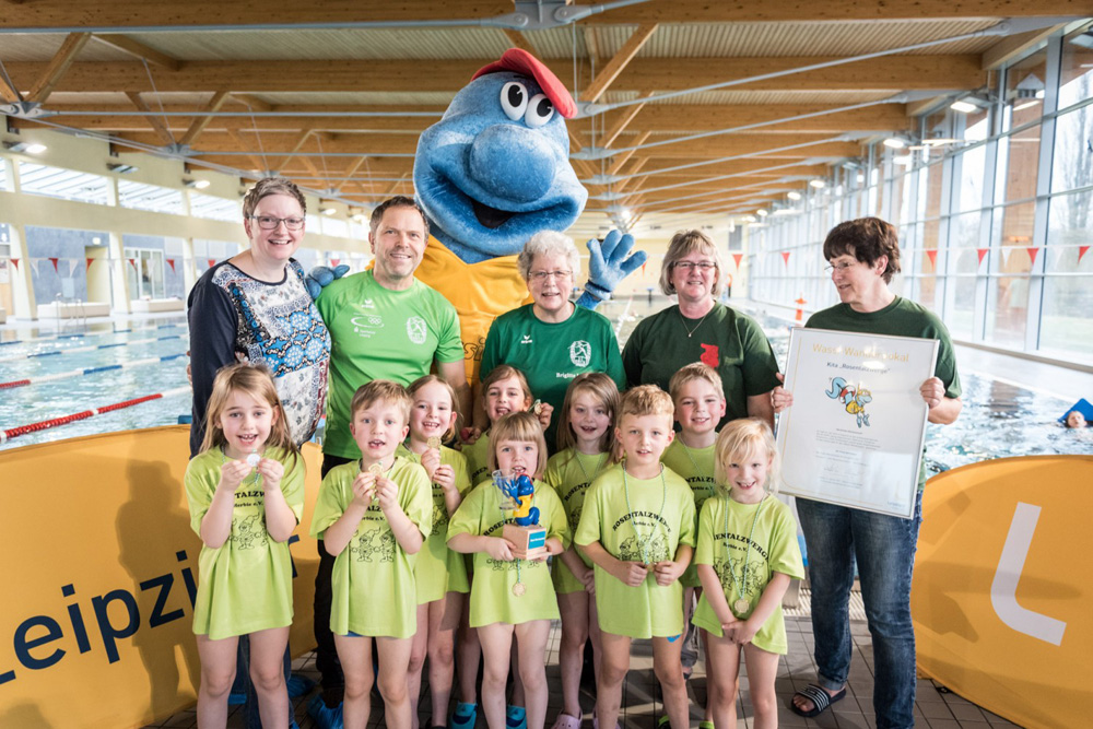 Siegreiche Kita: Die Rosentalzwerge aus dem Waldstraßenviertel haben den Wassi Wanderpokal 2016 gewonnen. Den Pokal nahmen sie von KWL-Maskottchen Wassi entgegen. Mit auf dem Foto; hintere Reihe v.l.: Katja Gläß (Pressesprechrin Wasserwerke), Steffen Matthes (SC DHfK), Schwimmtrainerin Brigitte Leonhardt sowie Sabine Hollrich und Petra Zillmann (Kita Rosentalzwerge). Foto: Leipziger Wasserwerke