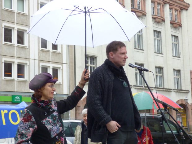 Das Wetter meinte es nicht gut: Initiatorin Barabar Rucha musste Michael Fischer-Art während dessen Ansprache den Regenschirm halten. Foto: Lucas Böhme