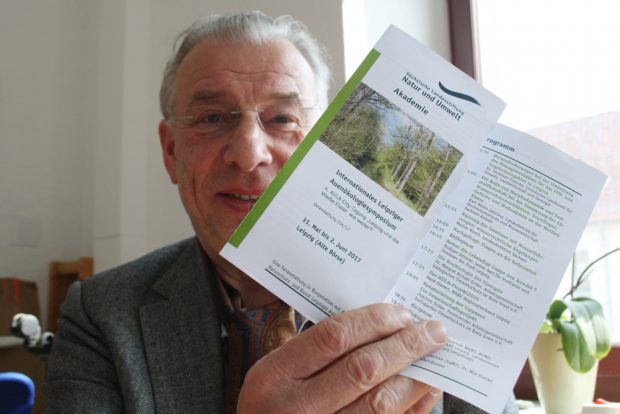 NuKLA-Vorsitzender Wolfgang Stoiber mit dem Flyer fürs Symposium. Foto: Ralf Julke