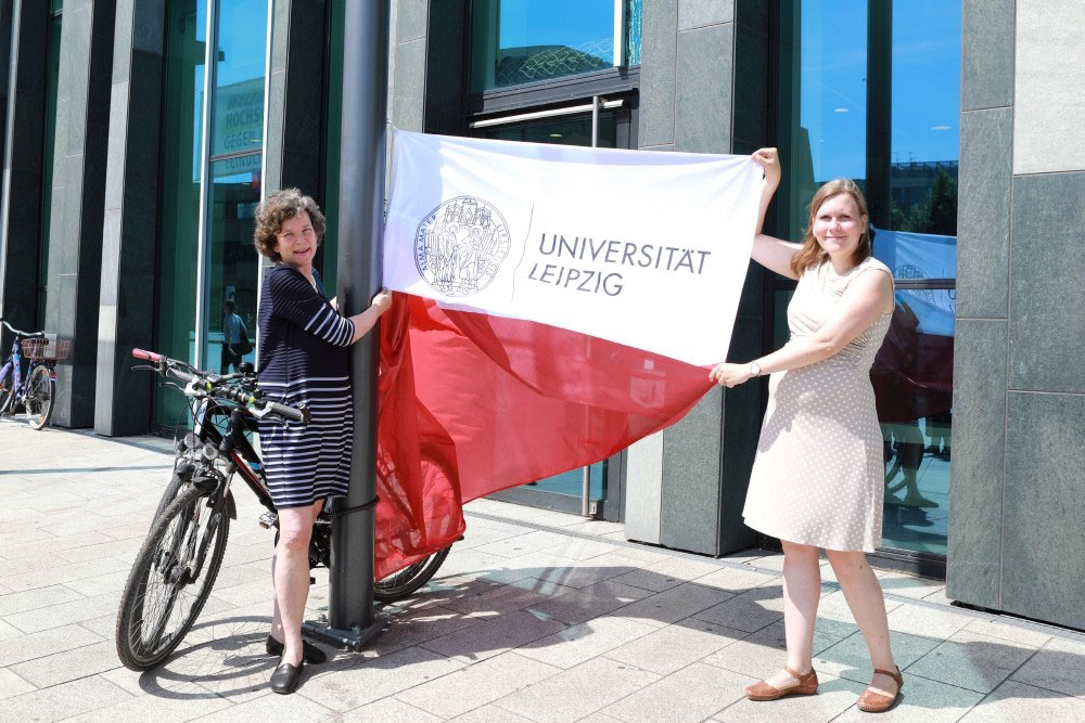 Rektorin Beate Schücking (links) und Madlen Mammen, Stabsstellenleiterin Universitätskommunikation, hissen vor dem Neuen Augusteum die Fahne mit dem neuen Logo. Foto: Swen Reichhold/Universität Leipzig