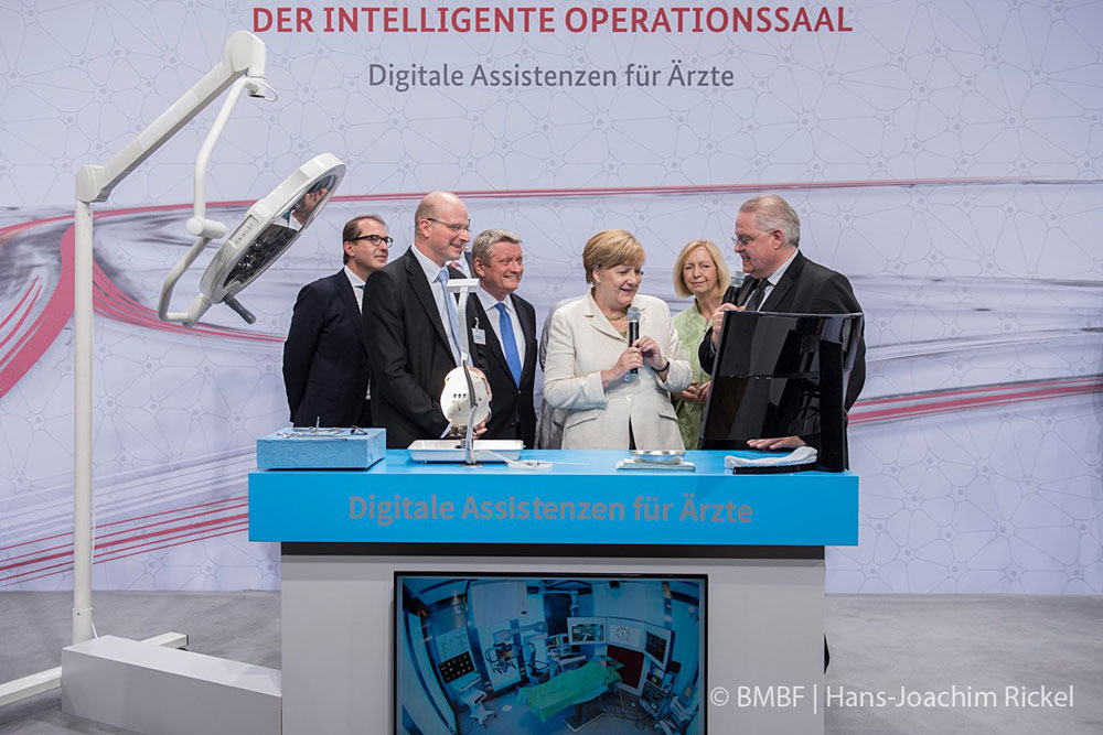 Thomas Neumuth (links) und Andreas Melzer (rechts) vom ICCAS der Universität Leipzig präsentieren der Bundeskanzlerin und weiteren Bundeskabinettsmitgliedern den intelligenten OP-Saal. Foto: Foto: BMBF/ Hans-Joachim Rickel