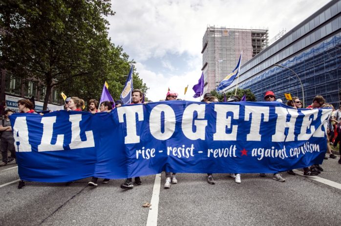 Block Transparent mit der Aufschrift: "All Together - rise -resist - revolt - against capitalism". Foto: Tim Wagner