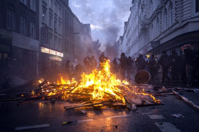 Brennende Barrikade am Eingang zum Schulterblatt, vom neuen Pferdemarkt kommend sowie Autonome im Hintergrund. Foto: Tim Wagner