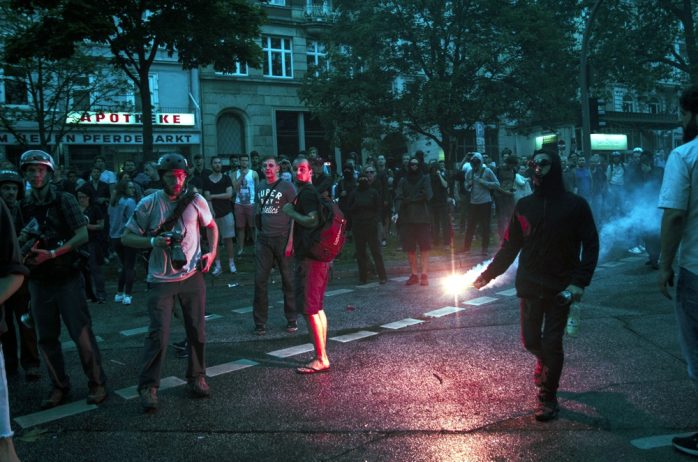 Vermummter rennt mit pyrotechnik, bengalischem feuer, welches rot Leuchtet richtung Schulterblatt. Foto: Tim Wagner