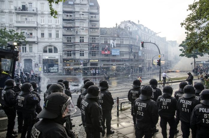 Polizei rückt am Neuen Pferdemarkt Richtung Schulterblatt mit Wasserwerfern vor. Im Hintergrund brennt eine Barrikade und Menschen stehen auf Hausdächern sowie einem Gerüst. Foto: Tim Wagner