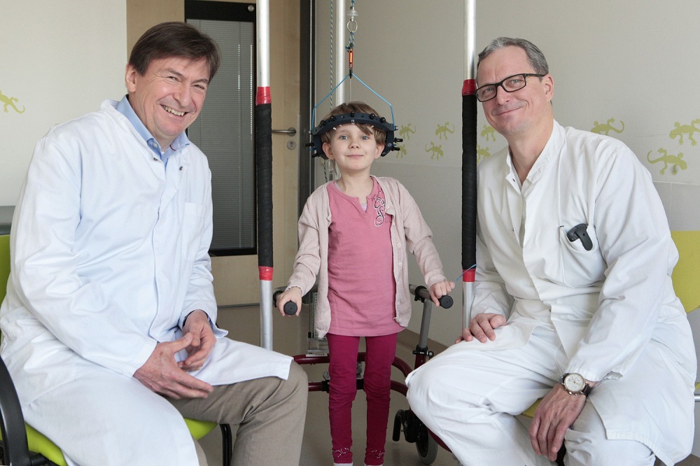 Prof. Christoph Heyde (re.), Leiter des neuen Kinderwirbelsäulenzentrums, und sein Stellvertreter, Prof. Jürgen Meixensberger (li.) mit der fünfjährigen Savannah. Ihre Wirbelsäule soll mit Gewichten, die an ihrem Kopf befestigt sind, in die richtige Form gebracht werden. Foto: Ines Christ / UKL