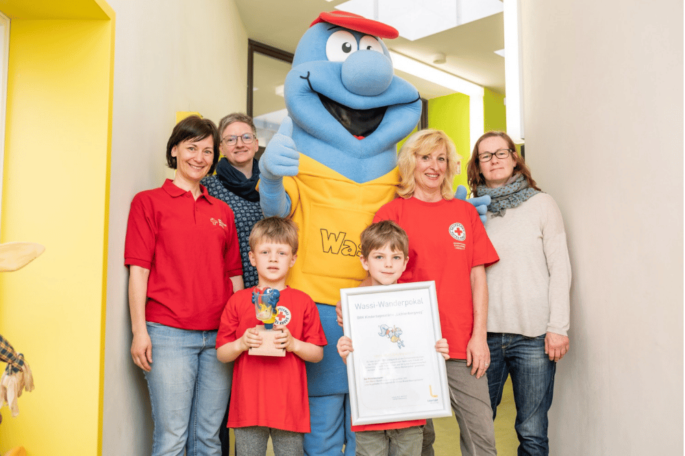 Glückliche Gewinner: Wasserwerke-Maskottchen Wassi überreichte Pokal und Urkunde an die Kita Lichtenbergweg. vorn v.l. in Rot: Heike Rehbock, die Schwimmkinder John und William, Sabine Peters aus der DRK-Kita; hinten v.l. Katja Gläß (Wasserwerke), Wassi, Annett Lüder (SC DHfK) Foto: Leipziger Gruppe