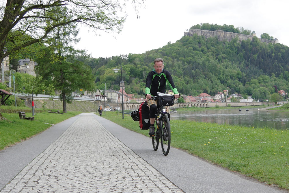 Oliver Pape am vierten Tag seiner Tour von Dessau bis zur tschechischen Grenze auf dem Elberadweg. Hier radelt der Berliner gerade durch das Städtchen Königstein in der Sächsischen Schweiz – im Hintergrund die berühmte Bergfestung. Foto: Hartmut Landgraf