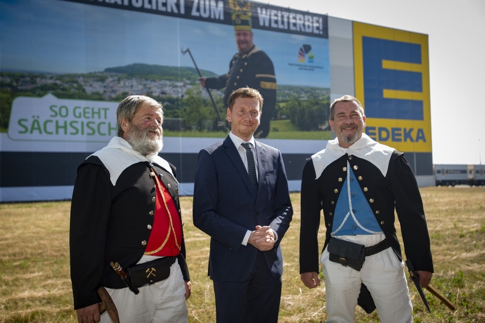 Ministerpräsident Michael Kretschmer (M.) steht mit den Kirchberger Bergbrüdern Wolfgang Prehl (l.) und Andre Prehl vor dem Megabanner. Quelle: Sächsische Staatskanzlei