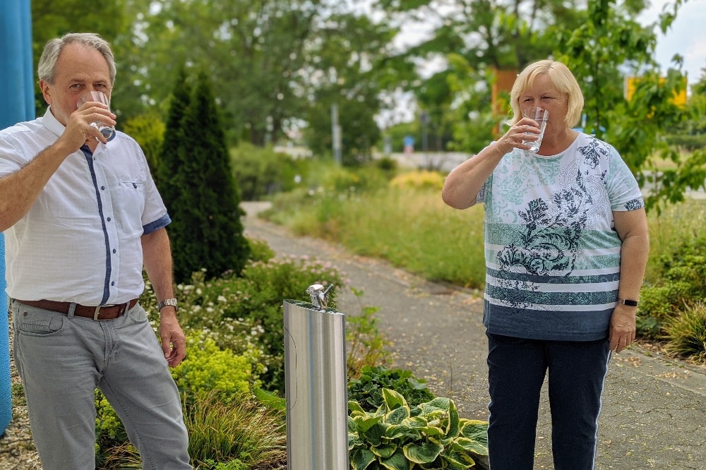 Mit Abstand und einem Glas Wasser: Geschäftsführer Dr. Peter Michalik und Ortsvorsteherin Beate Thiele trinken auf den neuen Trinkbrunnen in Weßnig. Quelle: Fernwasserversorgung Elbaue-Ostharz GmbH