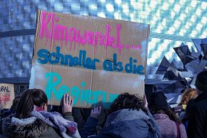 Mehrere Menschen auf einer Protestaktion von Fridays for Future. Zwei Personen halten ein Schild mit der Aufschrift "Klimawandel - schneller als die Regierung" in die Höhe