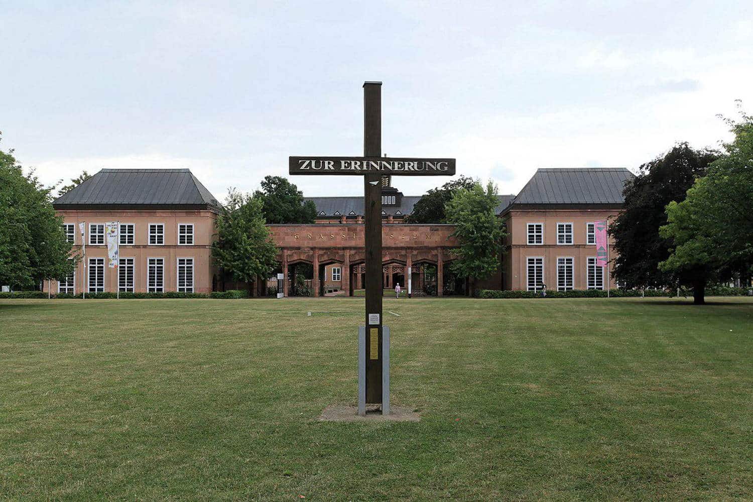 Mahnung und Erinnerung: Das Holzkreuz vor dem Grassimuseum. Foto: Frank Vincentz, GFDL, Quelle: https://commons.wikimedia.org/wiki/File:Leipzig_-_Johannisplatz_%2B_Erinnerungskreuz_%2B_Grassimuseum_01_ies.jpg