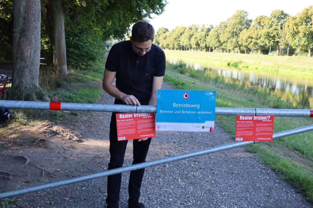 Linke-Stadtrat Michael Neuhaus bindet ein Protestschild an die Schranke auf dem Ratsholzdeich. Foto: Ralf Julke