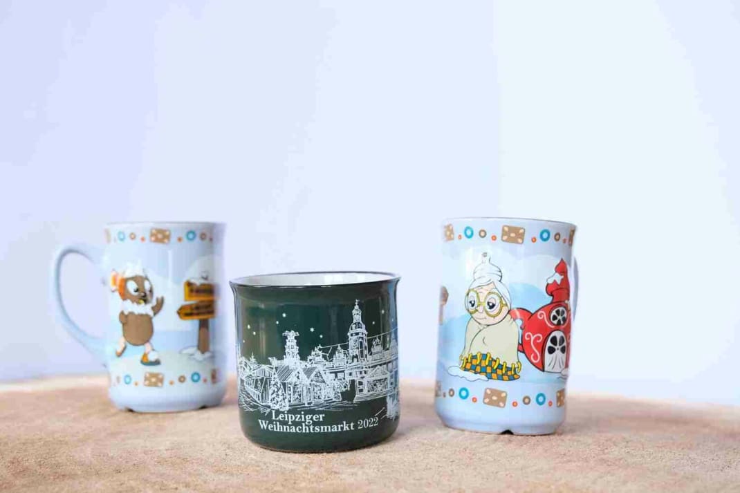 Die Tassen des Weihnachtsmarktes 2022 in drei verschiedenen Ausführungen. Eine mit Pittiplatsch, eine mit seiner Großmutter und eine mit Weihnachtsbäumen.