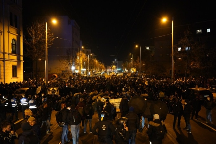 Hunderte Menschen stehen auf der Straße vor einer Gruppe Polizist*innen.