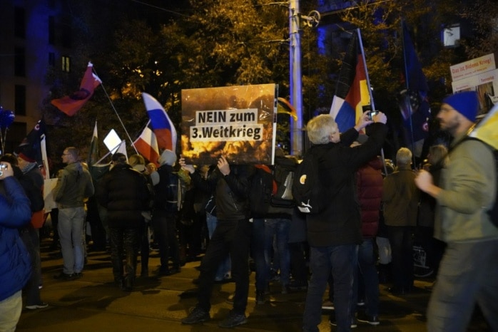 Hunderte Menschen stehen auf der Straße vor einer Gruppe Polizist*innen.