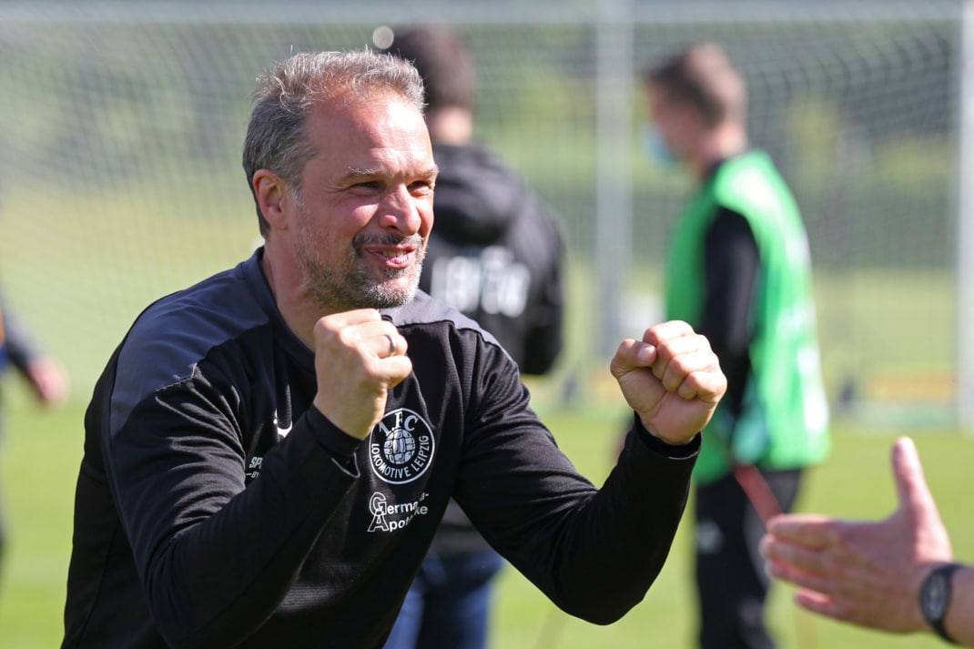 Der Cheftrainer des 1. FC Lok Leipzig, Almedin Civa, jubelt mit zwei angewinkelten Armen und geballten Fäusten. Im Hintergrund stehen zwei Spieler vor einem Fußballtor.