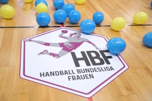 Blaue und gelbe Luftballons liegen auf und neben dem Logo der Handball Bundesliga Frauen (HBF) auf dem Spielfeld. Foto: Jan Kaefer
