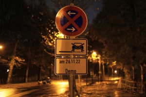 Ein Halteverbotsschild mit Zusatzschild "am 26.11. Demo" steht am Straßenrand. Im Hintergrund sind Polizeigitter an beiden Straßenrändern zu sehen.