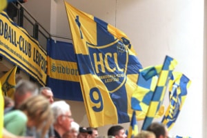 Blau-gelbe Fahnen mit dem Vereinswappen des HC Leipzig (HCL) im Fanblock. Foto: Jan Kaefer