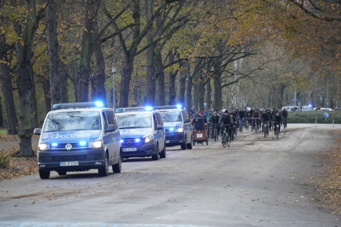 Über hundert Menschen fahren mit dem Fahrrrad auf einer Straße hinter Polizeifahrzeugen.