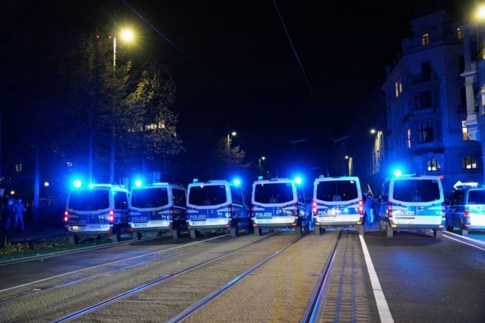 Eine dichte Polizeikette hindert Personen am Weiterlaufen, diese wir von Blaulicht angestrahlt.