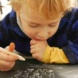 Ein kleines Kind mit einem Stift in der Hand vor einer Tafel, die auf dem Tisch liegt