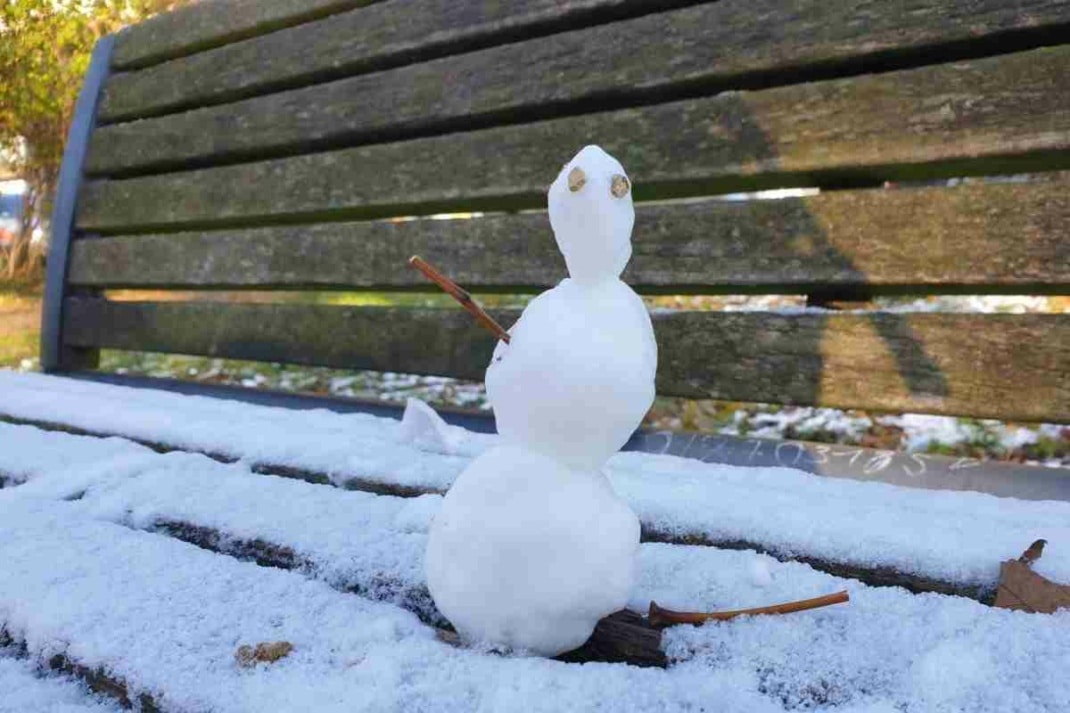 Ein kleiner Schneemann auf einer schneebedeckten Bank