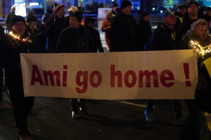 Demo-Teilnehmende tragen ein Banner mit der Aufschrift "Ami go home"