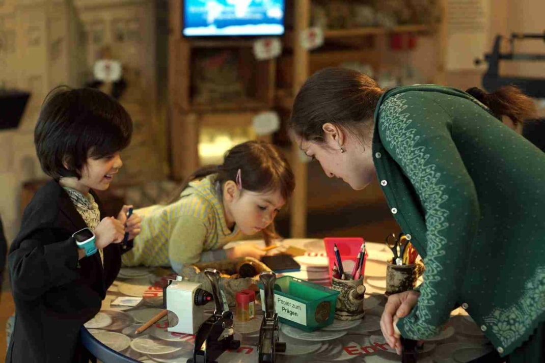 Blick ins Kindermuseum Leipzig. Zwei Kinder und eine Frau stehen an einem Basteltisch.