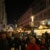 In der Grimmaischen Straße sind mehrere Stände des Weihnachtsmarktes zu sehen, im Hintergrund ein erleuchtetes Riesenrad. Dazwischen spazieren dutzende Menschen in zum Teil weihnachtlicher Kleidung.