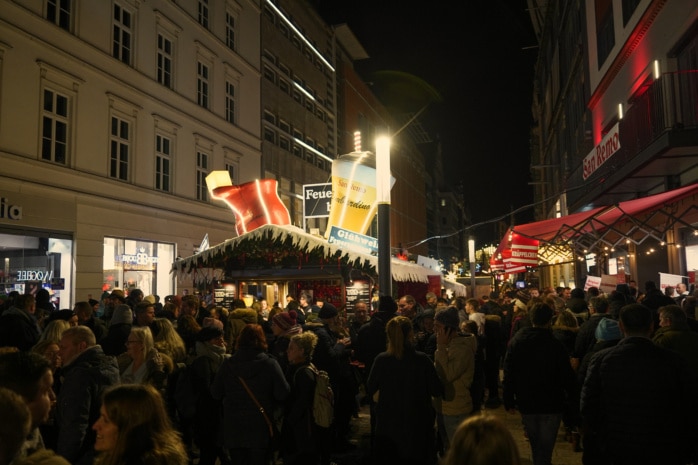 In der Grimmaischen Straße sind mehrere Stände des Weihnachtsmarktes zu sehen. Dazwischen spazieren dutzende Menschen in zum Teil weihnachtlicher Kleidung.