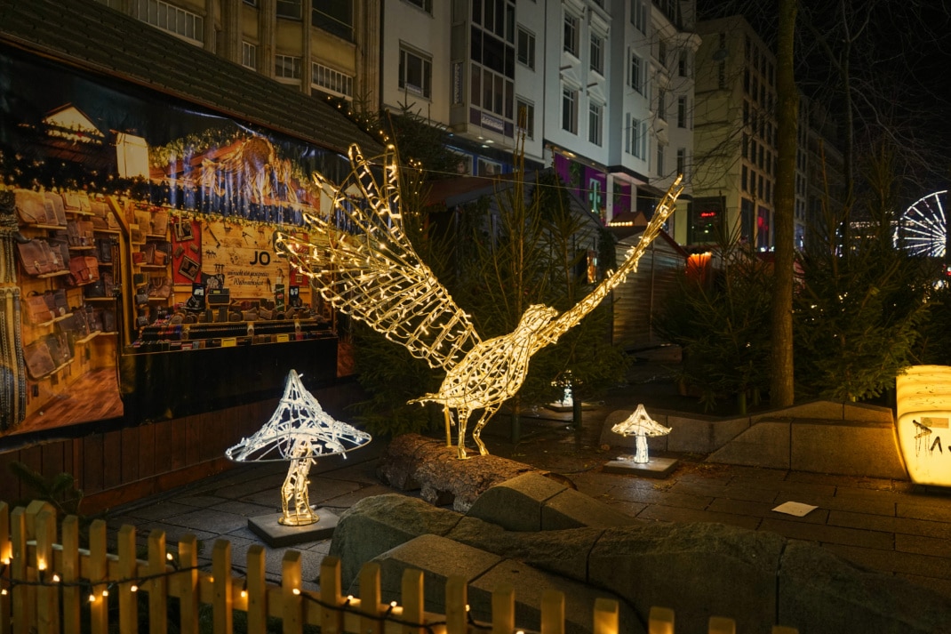 Ein aus Lichterketten geformter Fasan steht zwischen grünen Tannenbäumen auf dem Leipziger Weihnachtsmarkt.