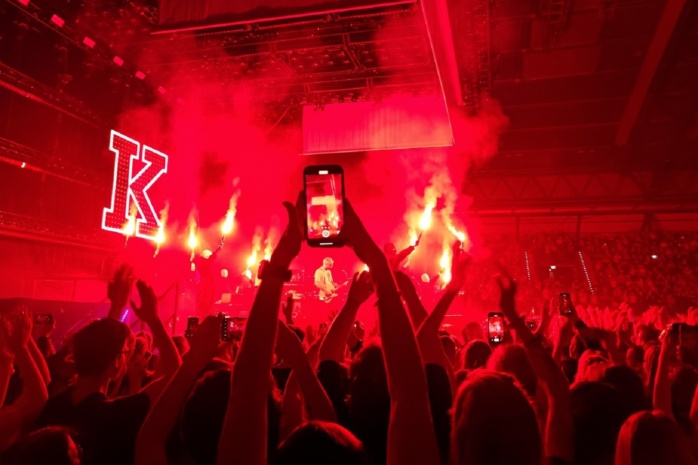 12.000 springende Fans beim Kraftklub-Konzert. Im Vordergrund eine Person, die mit dem Handy filmt. Im Hintergrund rotes Licht und Nebel vor dem K-Zeichen.