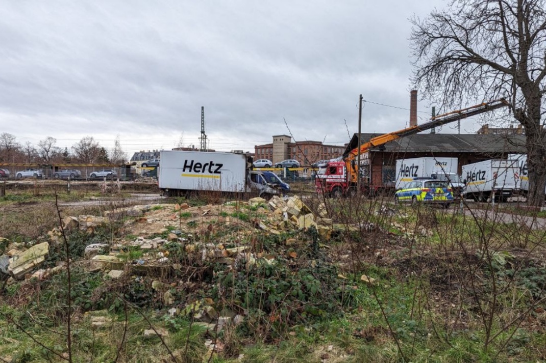 Ein Kran, ein Polizeiwagen und ein paar der abgebrannten LKWs auf dem Gelände der Firma