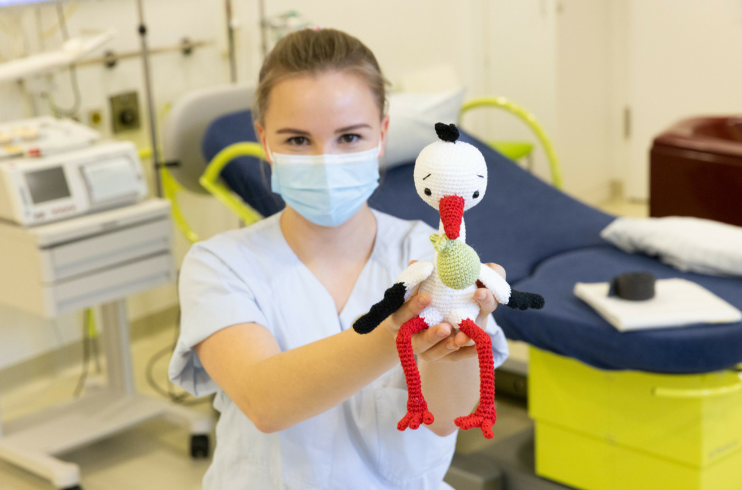 Eine Hebamme im Behandlungszimmer hält einen Stofftierstorch in die Kamera