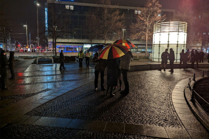 Drei Menschen stehen mit Regenschirmen auf dem Augustusplatz