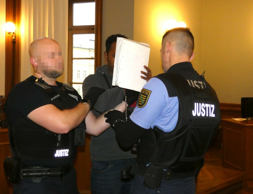 Der Angeklagte im Gerichtssaal mit zwei Beamten