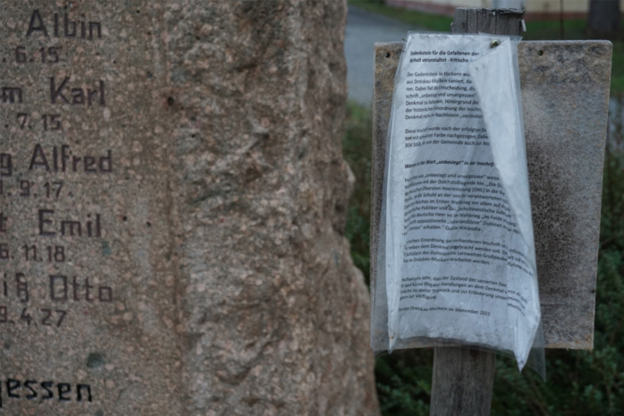 Ein Erklärungszettel in einer Klarsichthülle hängt an einem Gedenkstein
