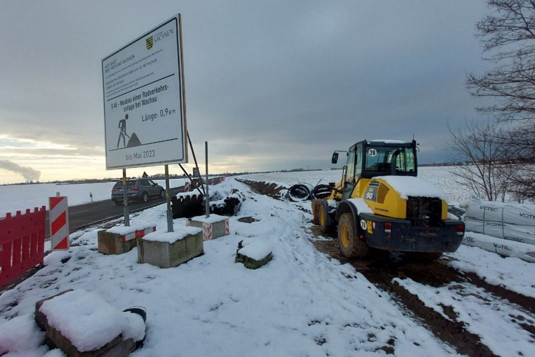 Bagger neben Baustellentafel im Schnee.