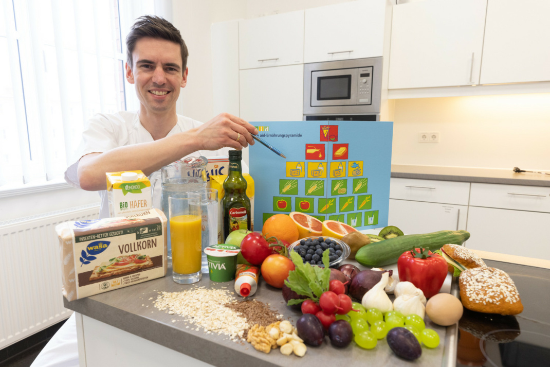 Lars Selig, Leiter des UKL-Ernährungsteams, mit einer Ernährungspyramide, davor liegt Obst und Gemüde.