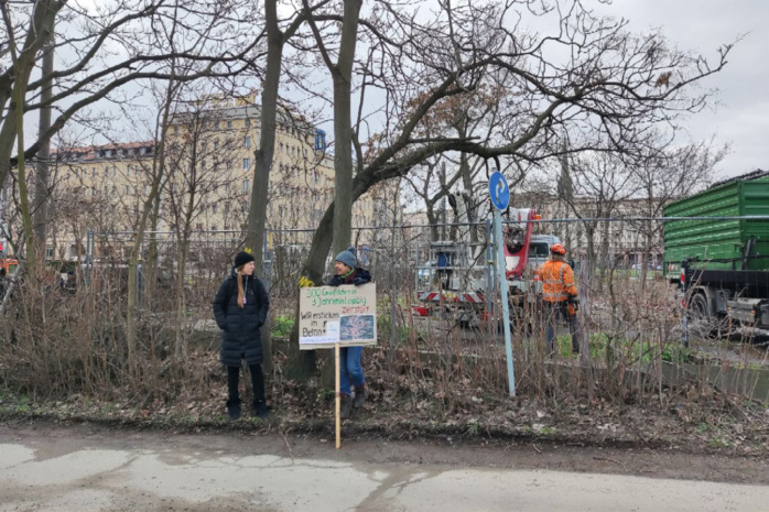 Personen vor einem Zaun am Leipziger Wilhelm-Leuschner-Platz mit Protestschild