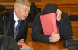 Angeklagter verdeckt Gesicht neben Anwalt.