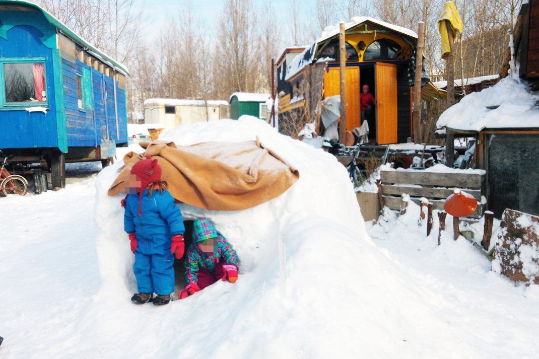 Kinder spielen im Schnee, im Hintergrund sind Bauwagen zu sehen.