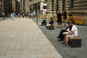 Menschen sitzen am Eingang zur Petersstraße auf Bänken.