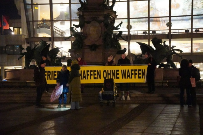 Personen vor einem Banner, auf dem steht "Frieden schaffen ohne Waffen"