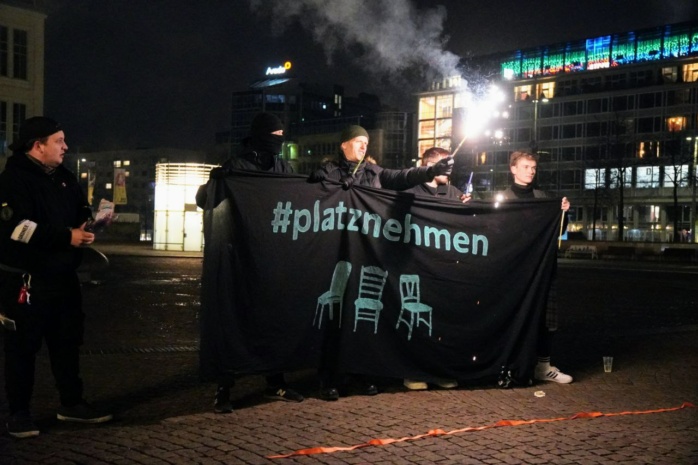 Personen mit einem Banner mit der Aufschrift "Platznehmen", die Pyrotechnik halten